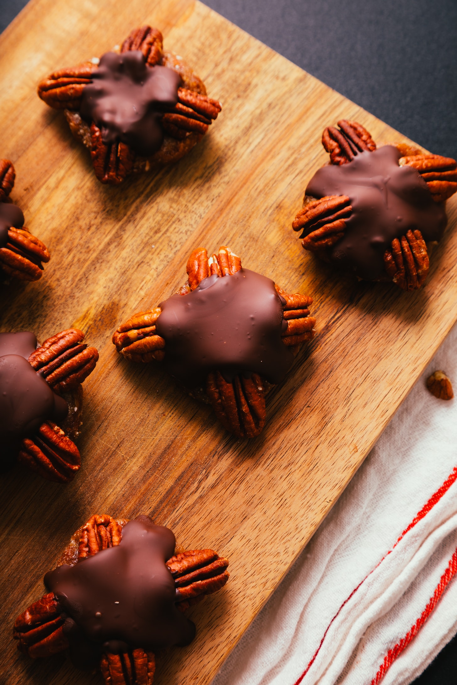 Cutting board with homemade vegan turtle candies made with pecans, dates, and dark chocolate