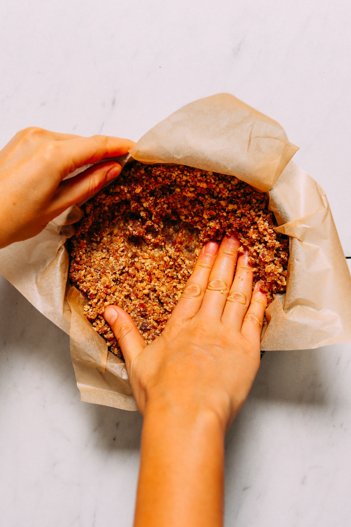 Pressing the walnut date no-bake cheesecake crust into a parchment-lined pan