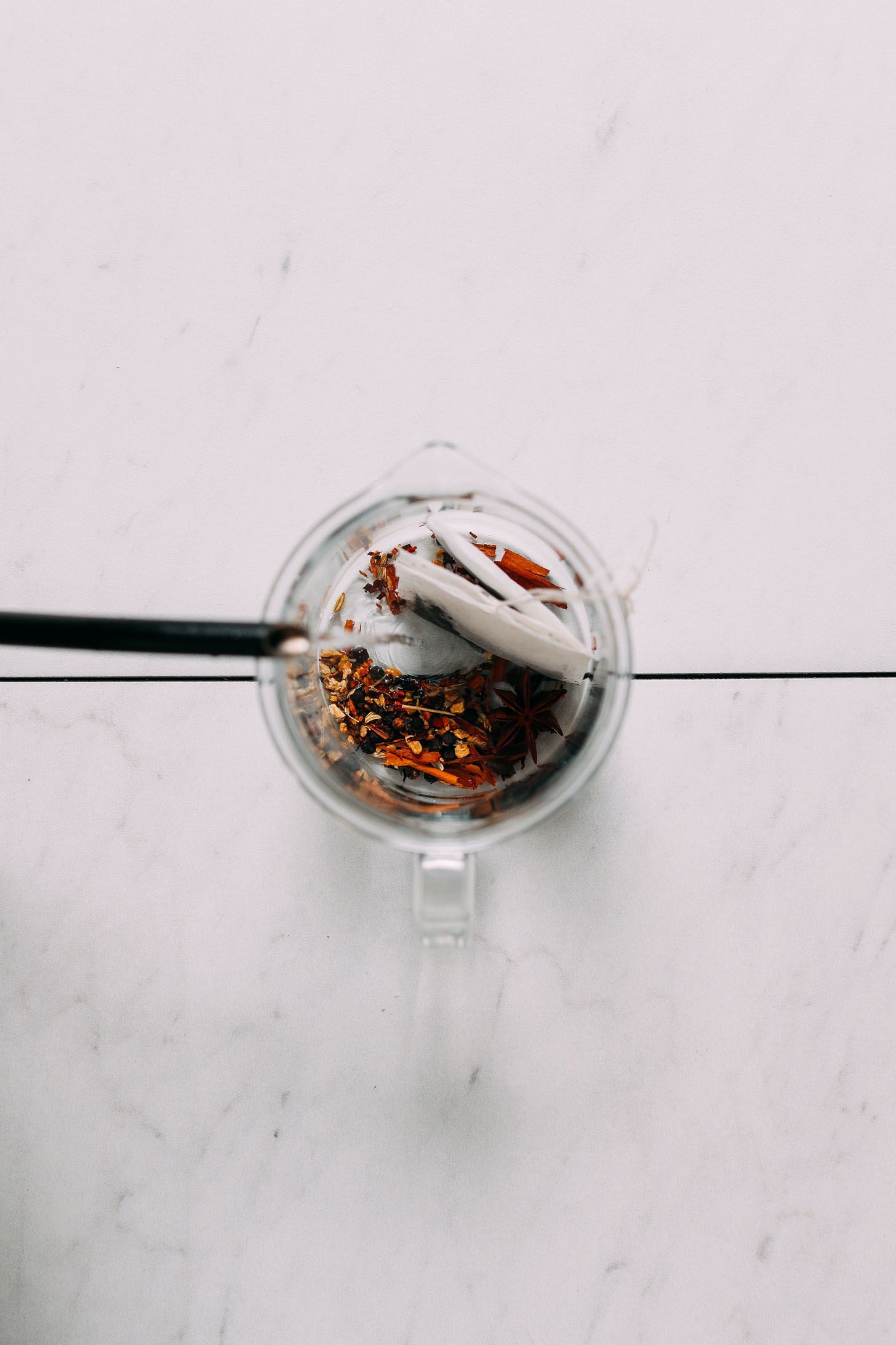 Overhead image of hot water being poured over black tea and spices in a clear jar