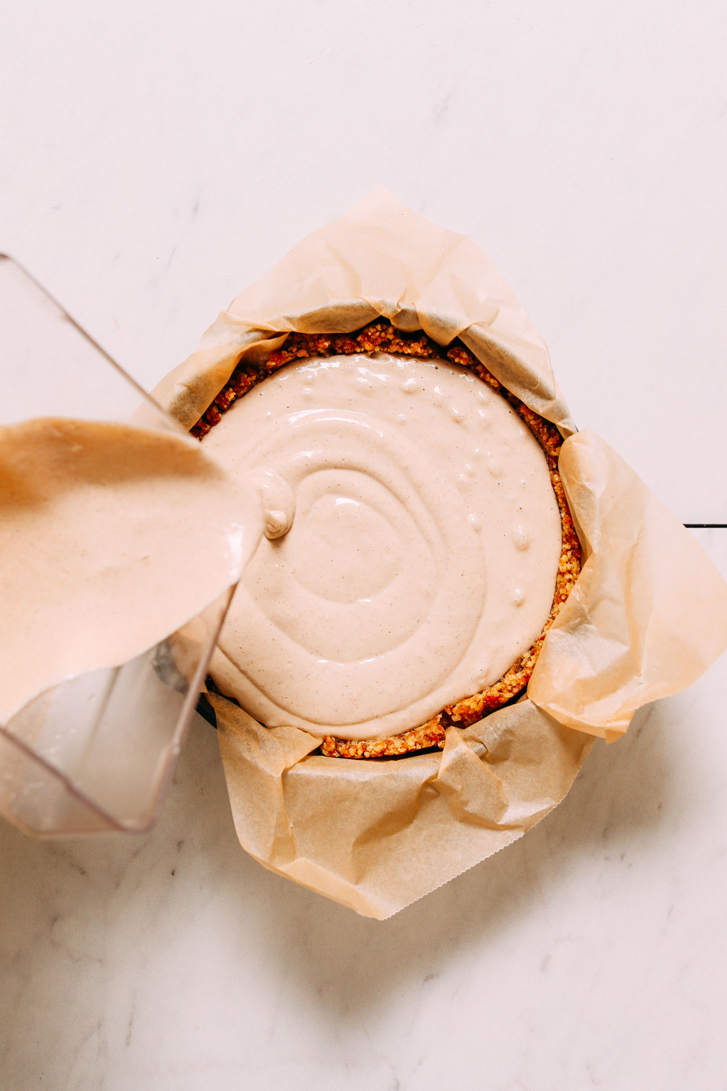 Pouring Vegan Cheesecake filling into a walnut-date crust