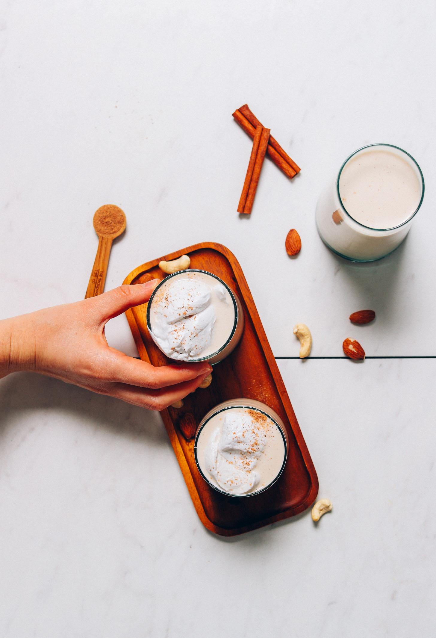 Holding onto a glass of Easy Vegan Eggnog topped with coconut whipped cream