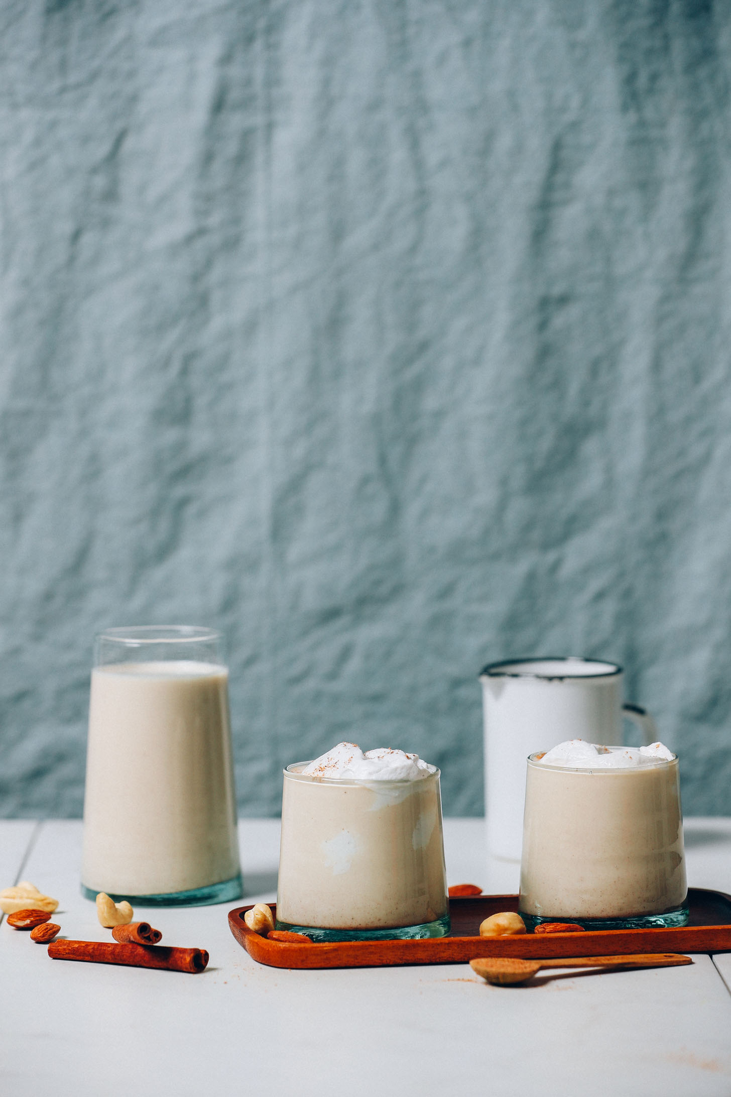 Glasses of Vegan Eggnog on and next to a wood tray with cashews and almonds