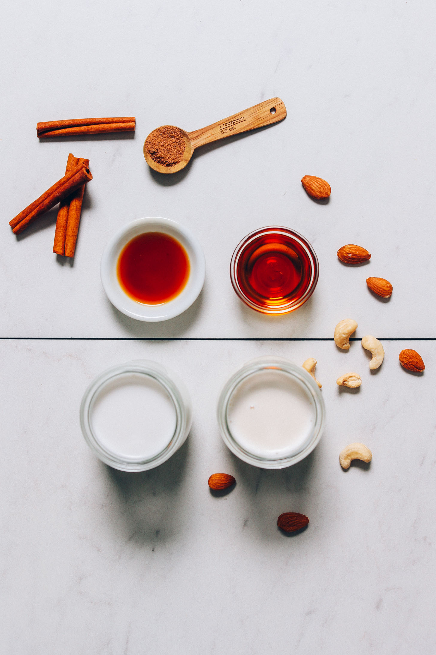 Cinnamon sticks, maple syrup, dairy-free milk, and other ingredients for making our Easy Vegan Eggnog recipe