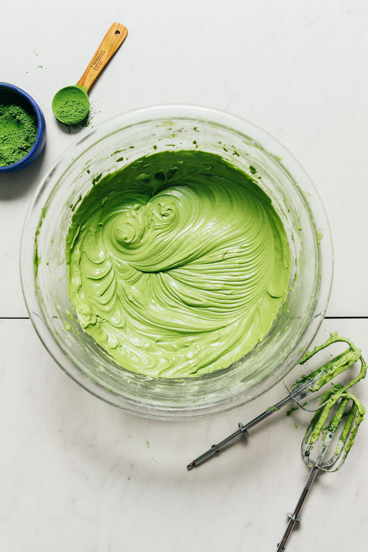 Bowl of Vegan Matcha Buttercream Frosting beside hand mixer blades