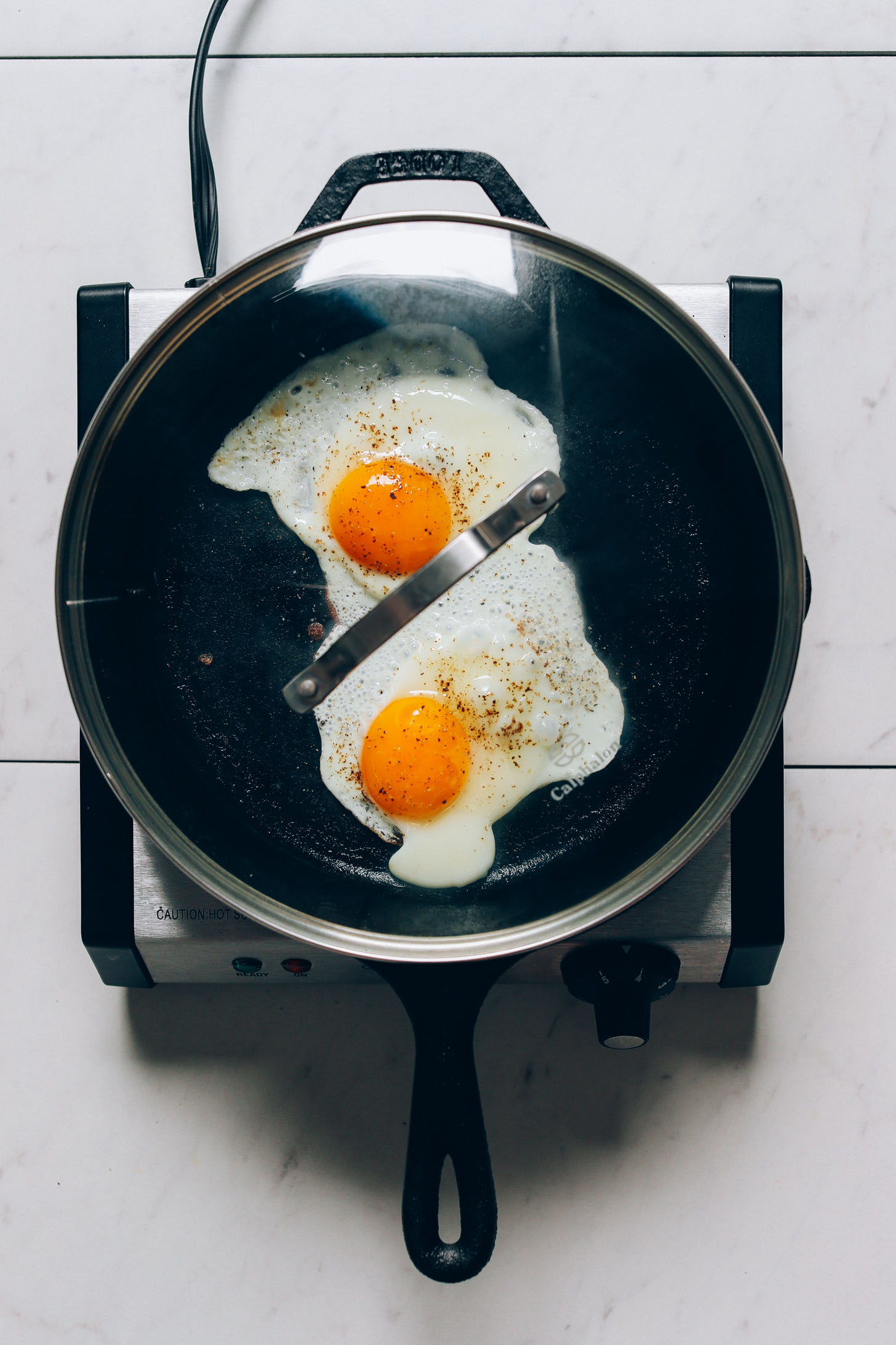 Cooking fried eggs with a lid on for our tutorial on How to Cook and Egg