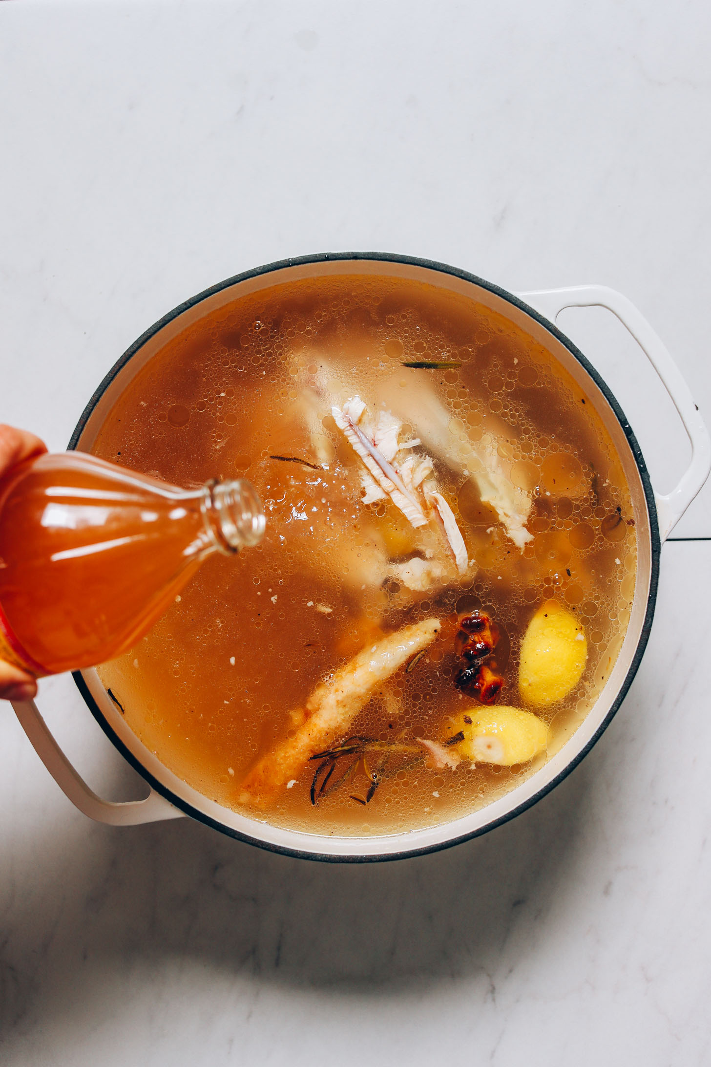 Pouring apple cider vinegar into a pot to help release nutrients from the chicken bones