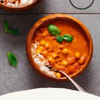 Bowls of Chickpea Tomato Peanut Stew with rice and topped with fresh basil