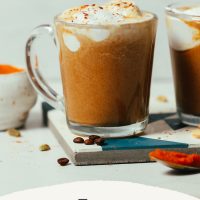 Mugs of our Easy Pumpkin Spice Latte recipe topped with coconut whipped cream and pumpkin pie spice