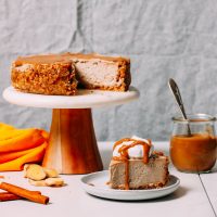 Slice of Vegan Chai Cheesecake next to a jar of caramel sauce and the remaining cheesecake