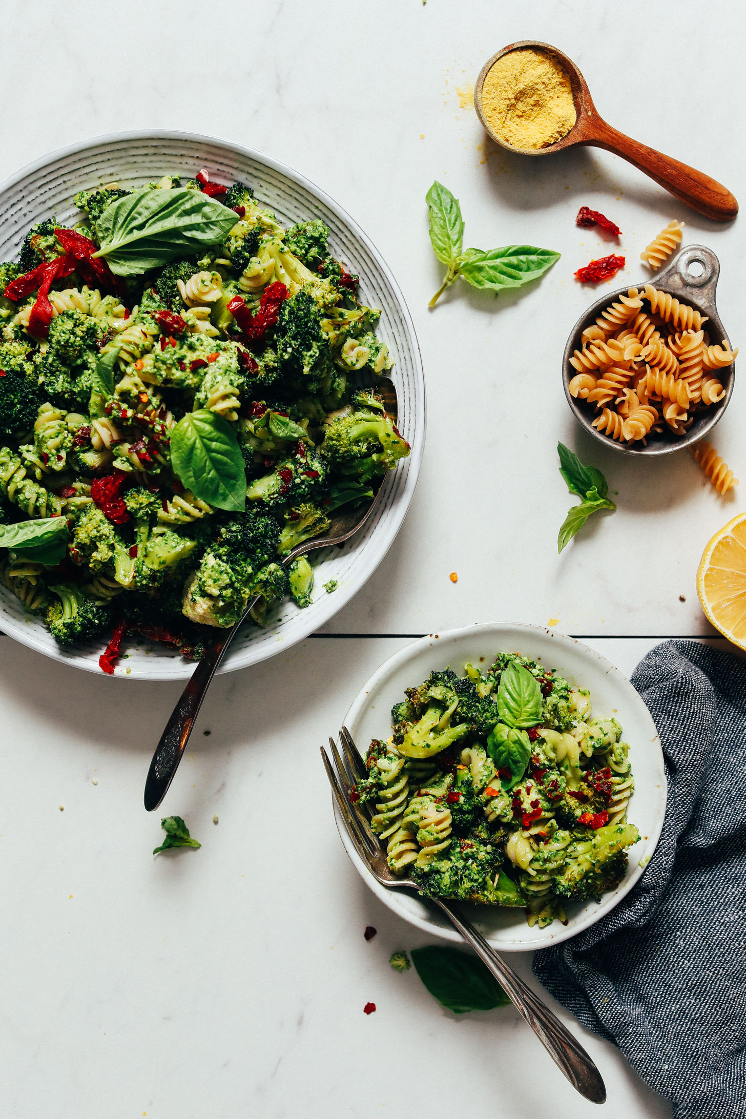 Gluten-free noodles and nutritional yeast beside bowls of our Roasted Broccoli & Pasta Salad with Hemp Pesto