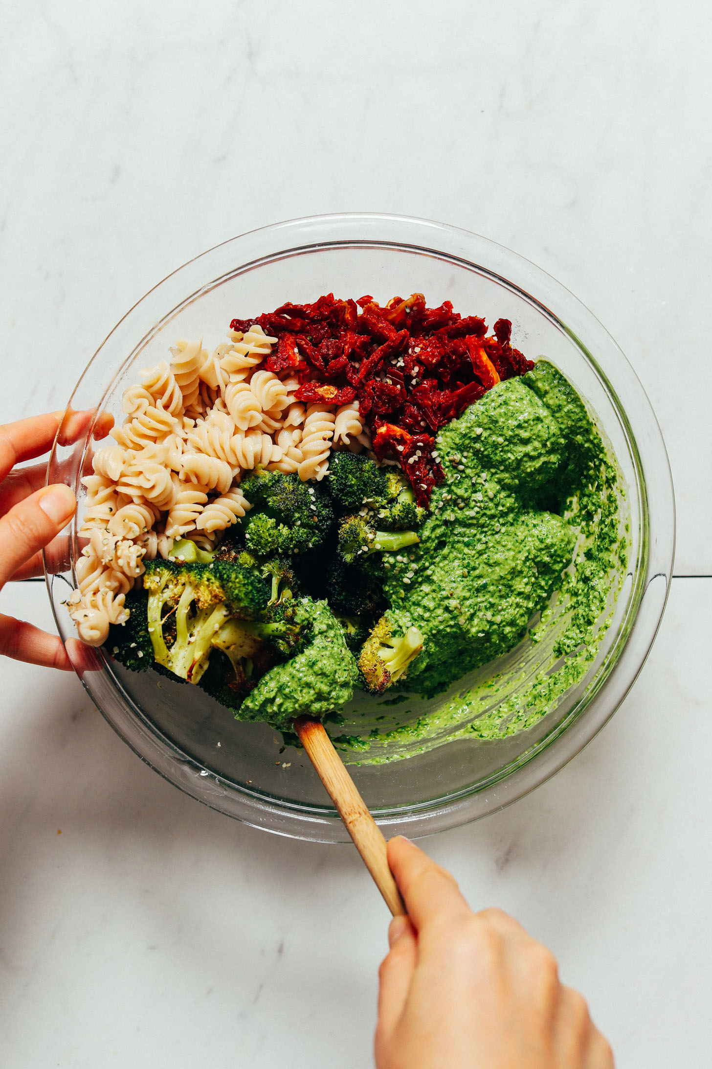 Using a wooden spoon to stir a bowl of Roasted Broccoli and Pesto Pasta Salad