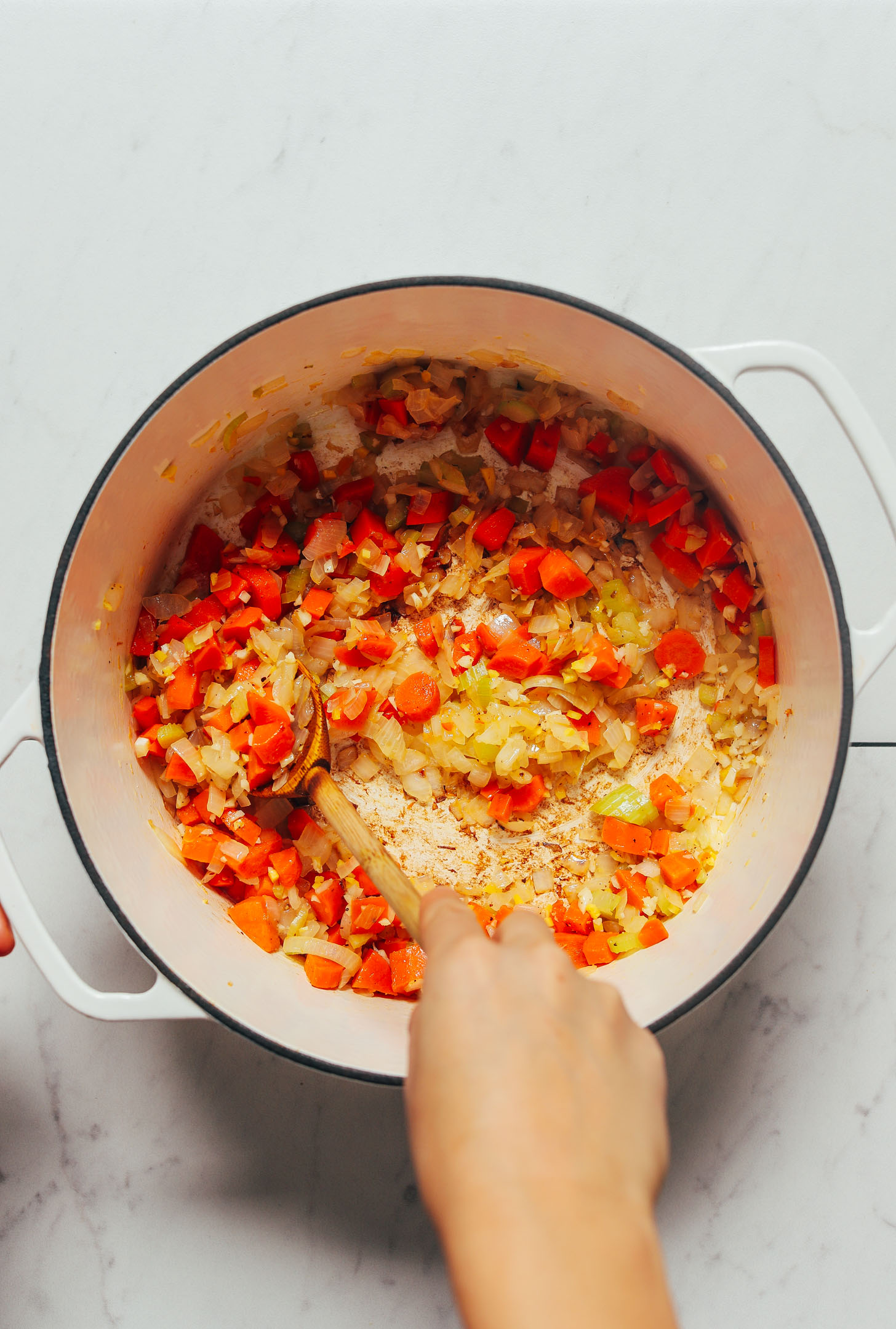 Using a wooden spoon to stir oninos, carrot, celery, and garlic for our Curried Cauliflower Lentil Soup recipe