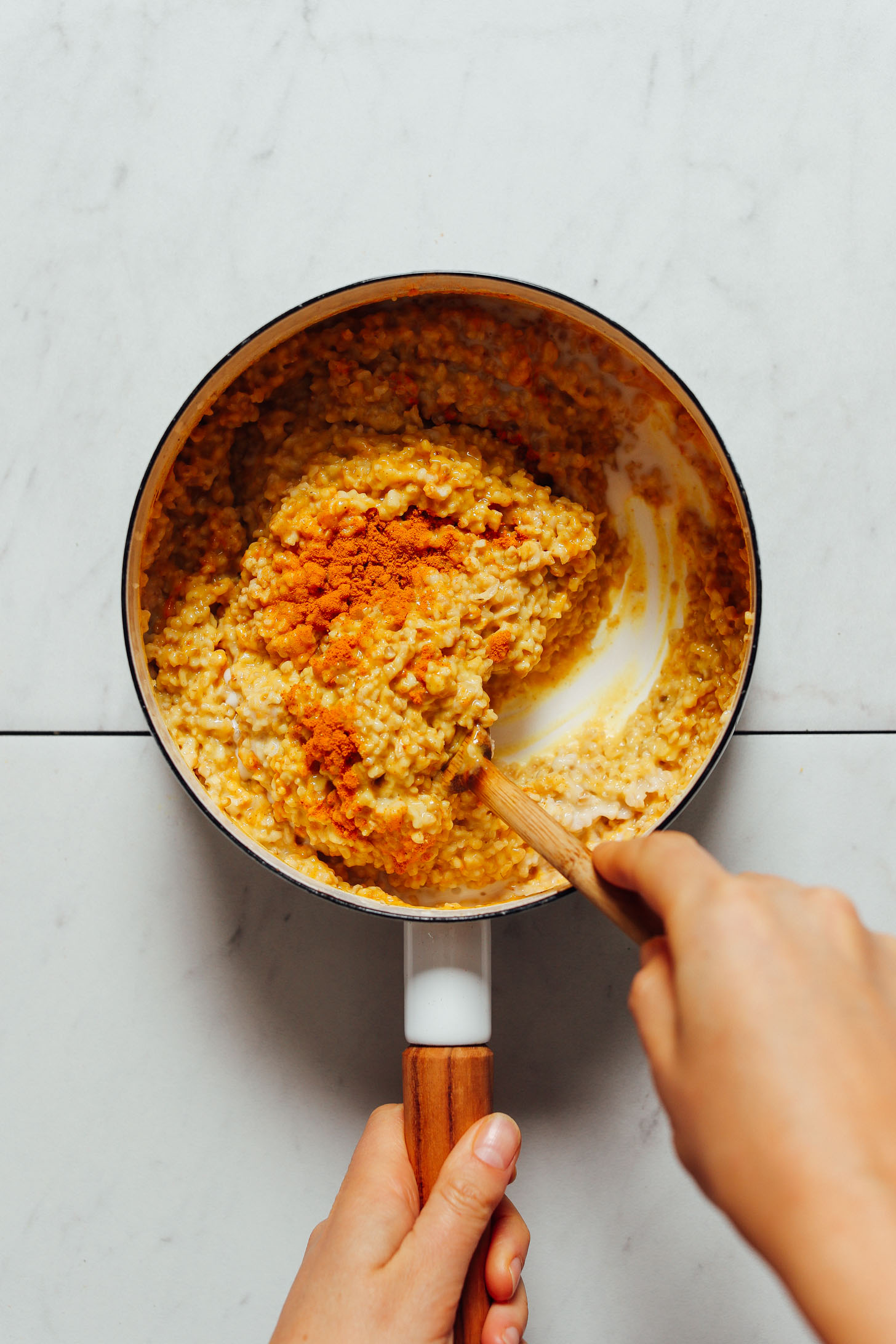 Using a wooden spoon to stir a saucepan of Turmeric Porridge