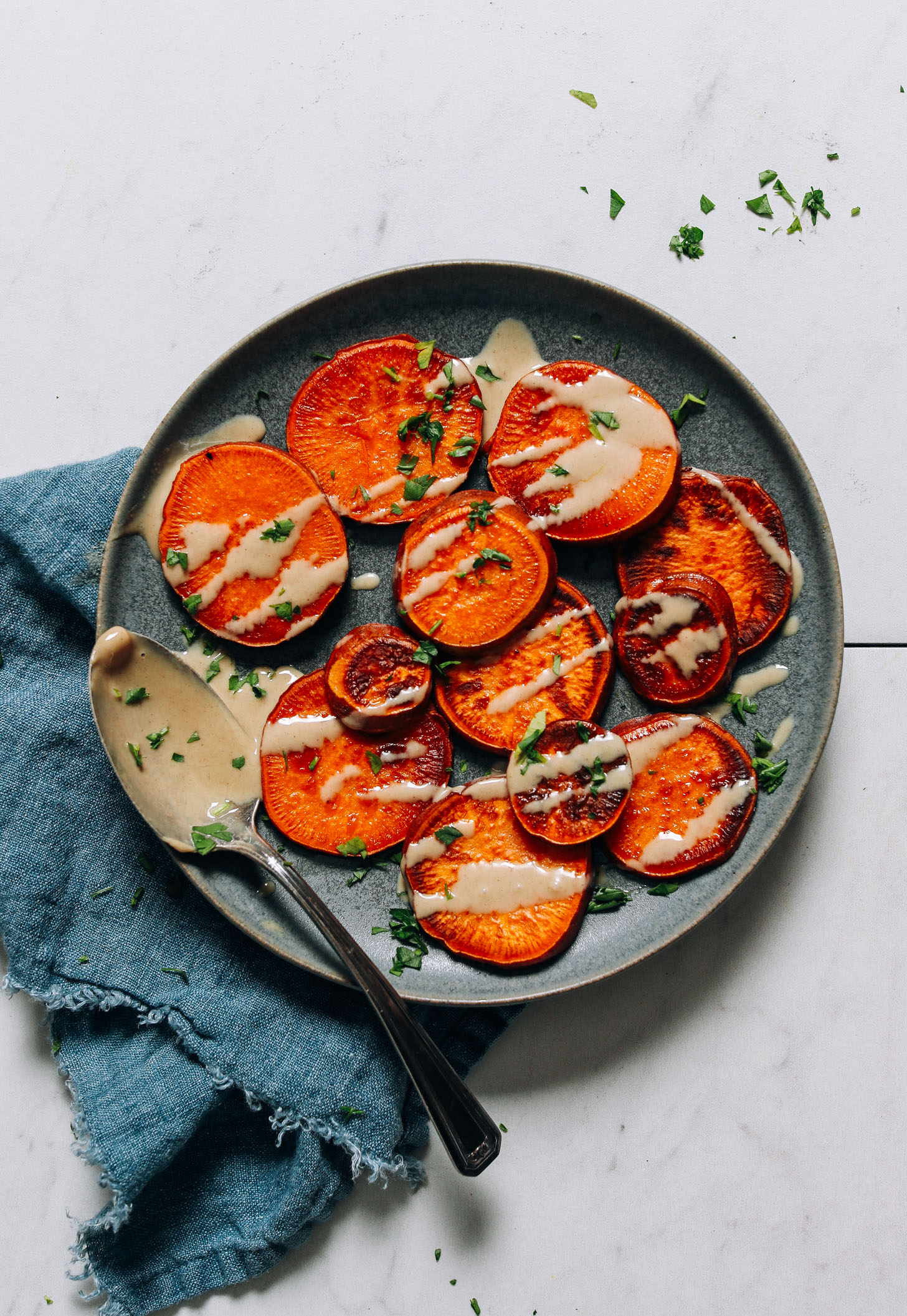 Plate of sliced sweet potatoes drizzled with tahini and parsley