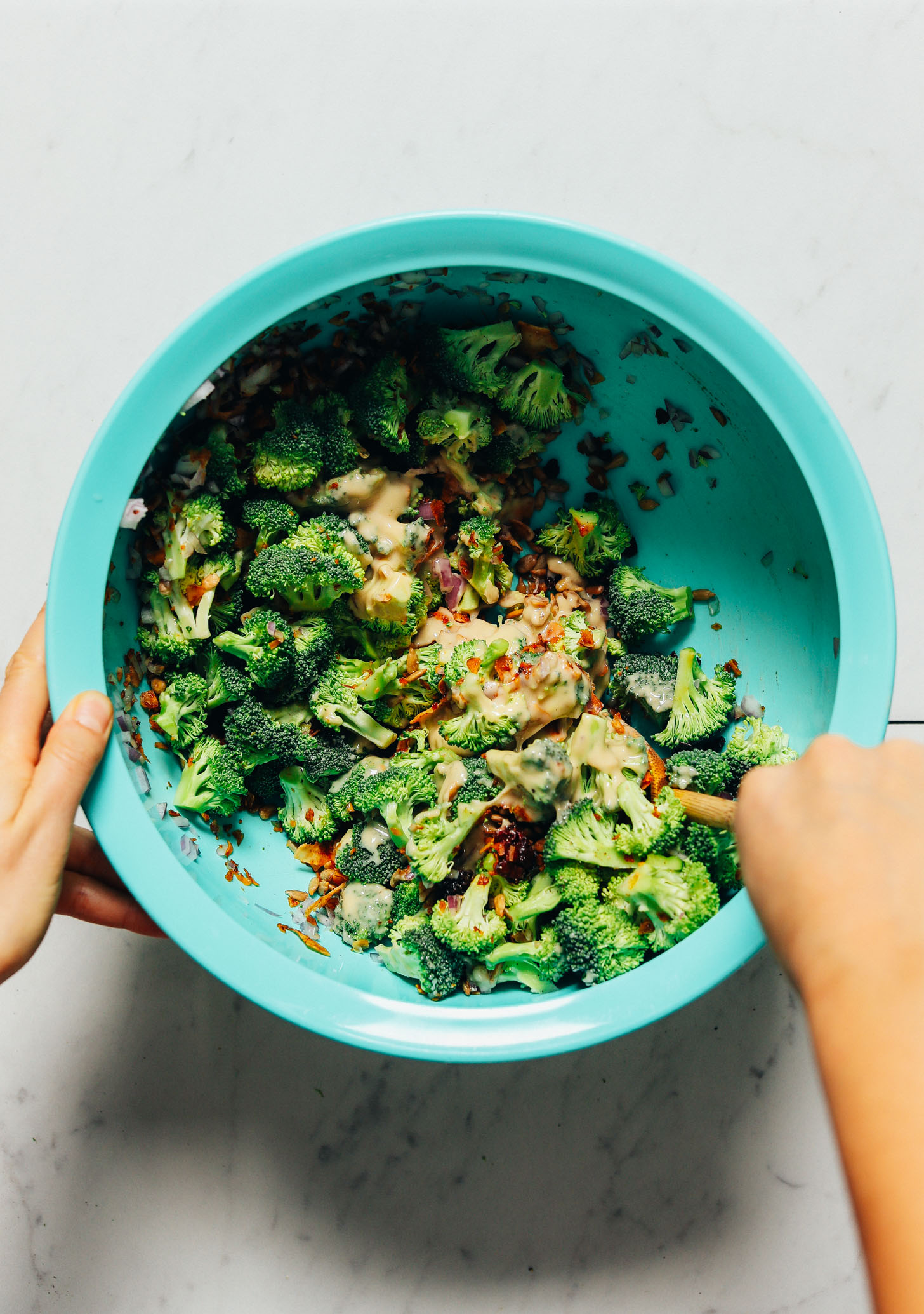 Using a wooden spoon to stir a mixing bowl of Creamy Vegan Broccoli Salad