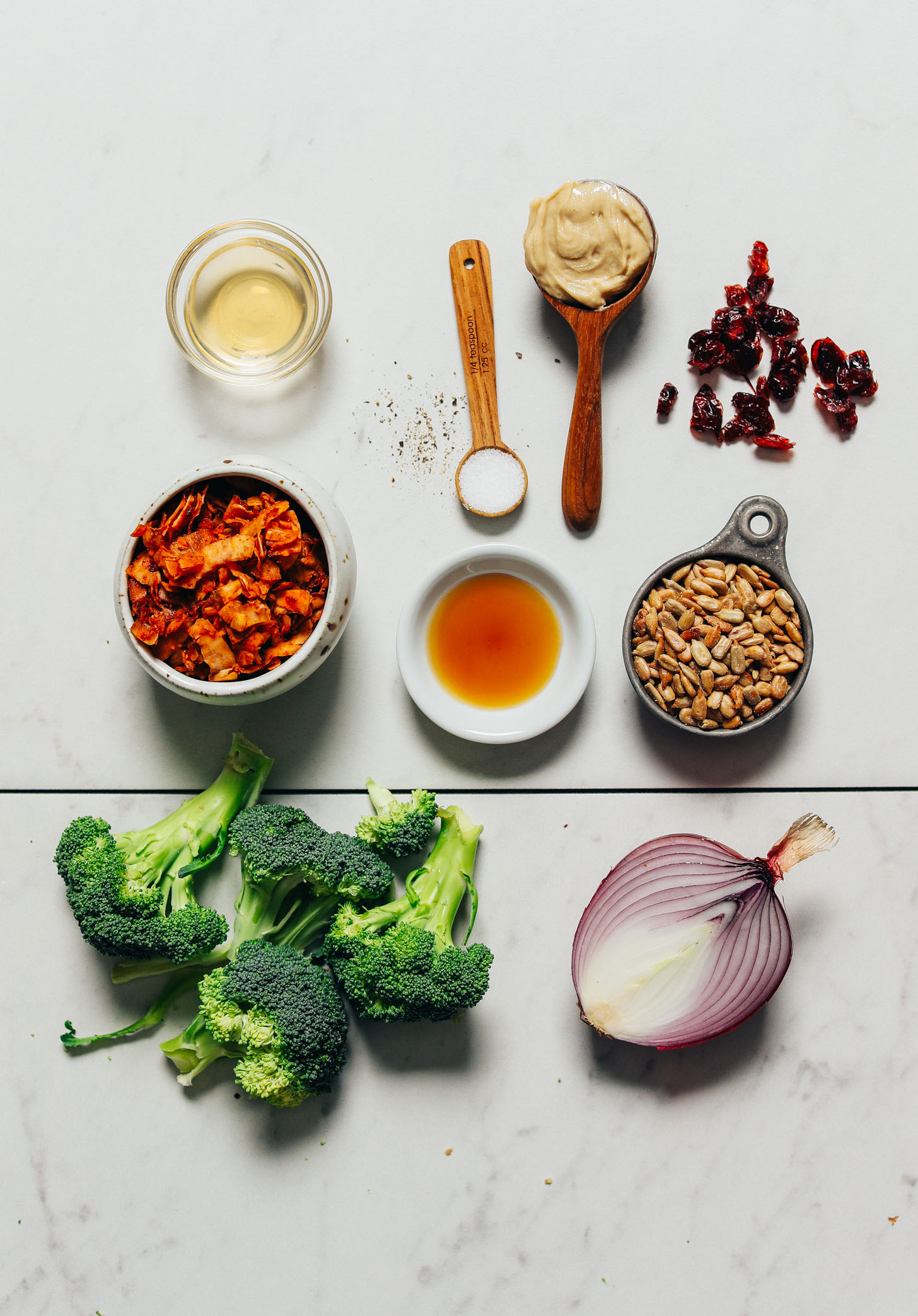 Red onion, broccoli, coconut bacon, sunflower seeds, cashew butter, and other ingredients for making our Creamy Vegan Broccoli Salad recipe