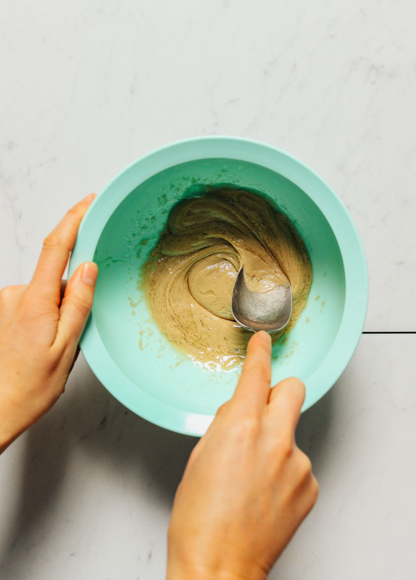 Using a spoon to stir a bowl of tahini dressing for kale salad