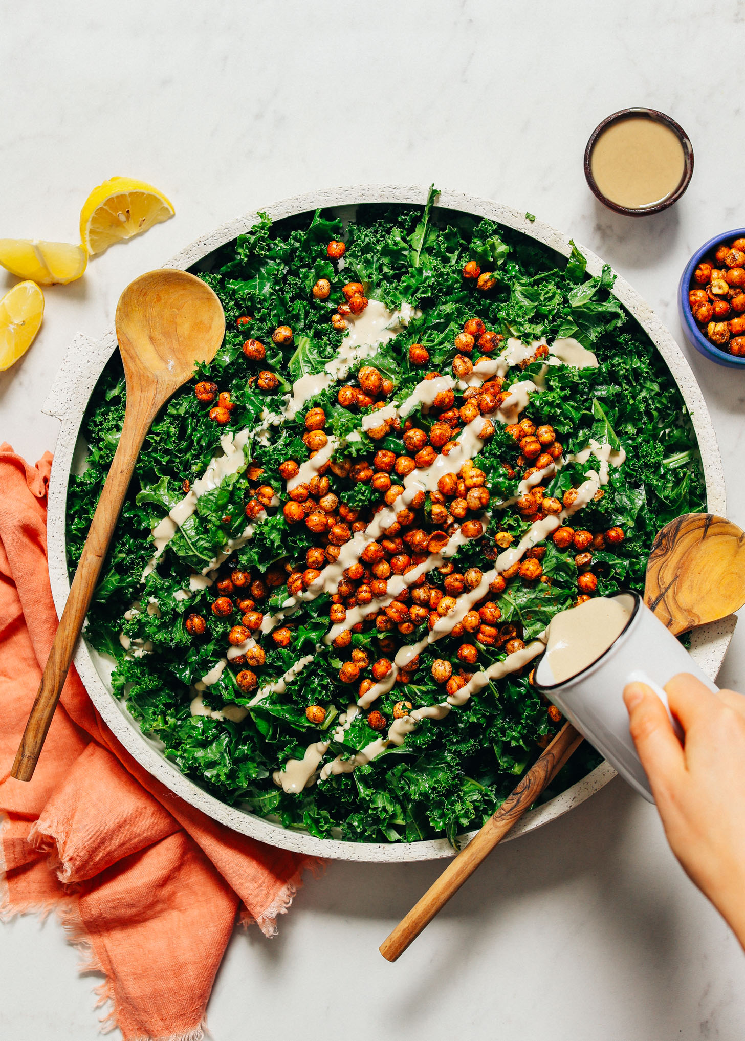 Pouring tahini dressing from a small pitcher onto kale salad