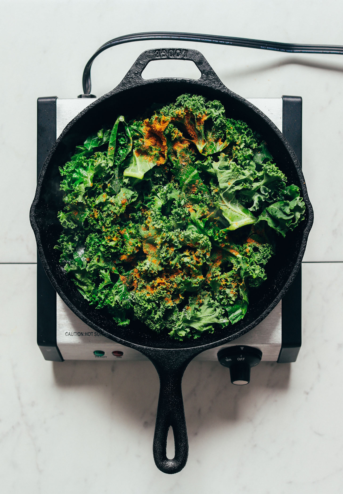 Skillet filled with kale and sprinkled with curry powder