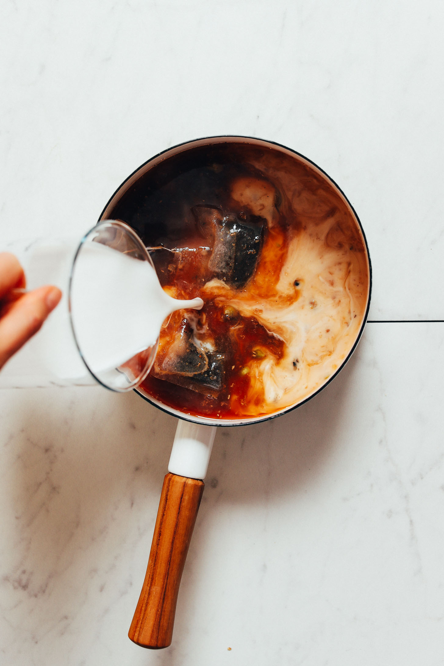 Pouring dairy-free milk into a saucepan to make our Masala Chai recipe