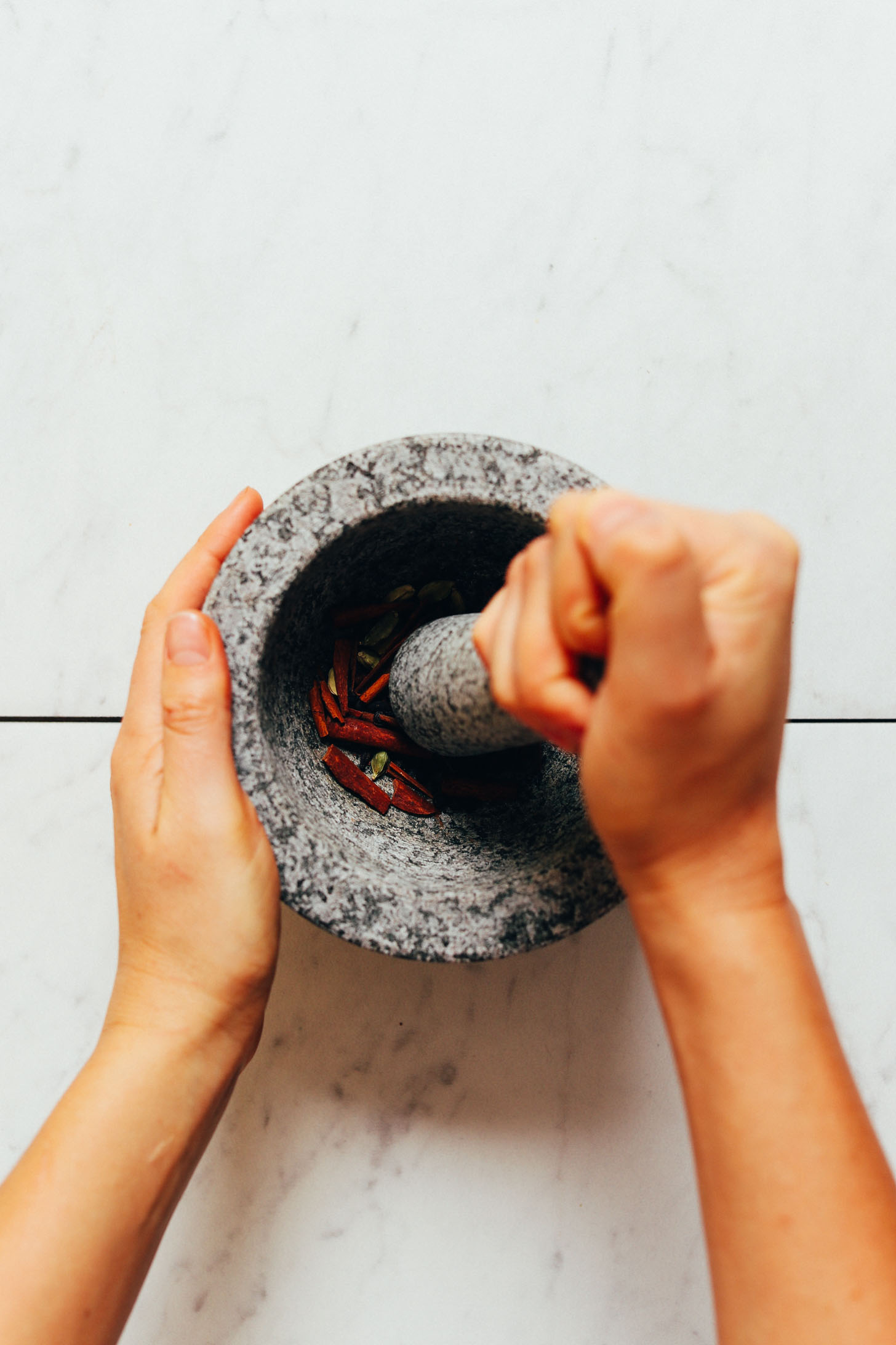 Using a mortar and pestle to slightly grind whole spices for making homemade Chai Tea