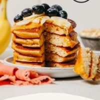 Bite removed from a stack of Gluten-Free Blender Banana Pancakes topped with fresh blueberries and banana