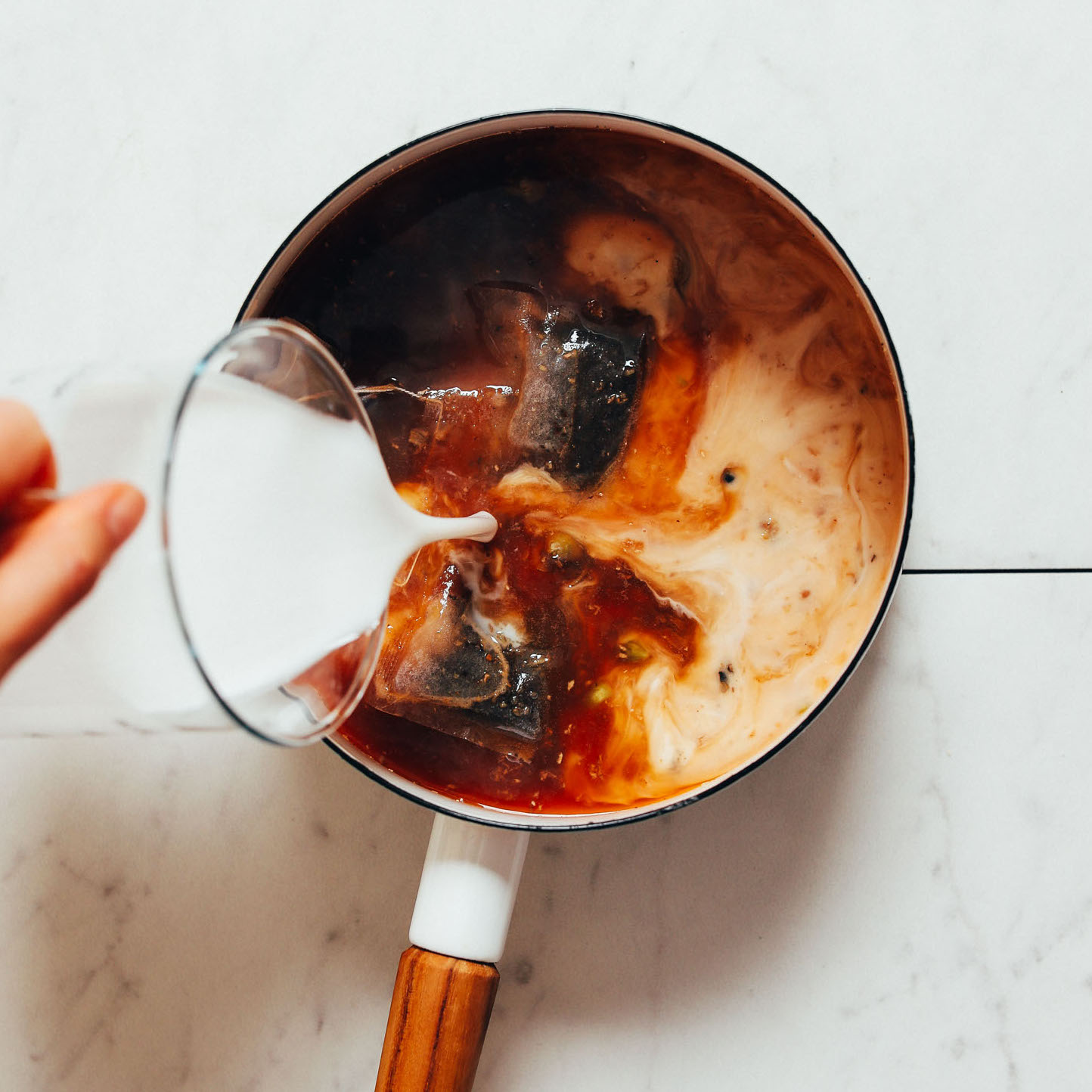 Pouring dairy-free milk into a saucepan of homemade Masala Chai