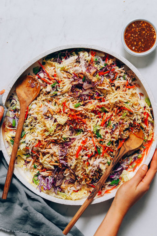 Holding a large serving dish filled with a batch of our Chinese Chicken Salad recipe