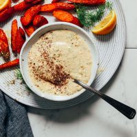roasted carrots plated with a bowl of creamy garlic dill sauce and a fresh dill and lemon garnish