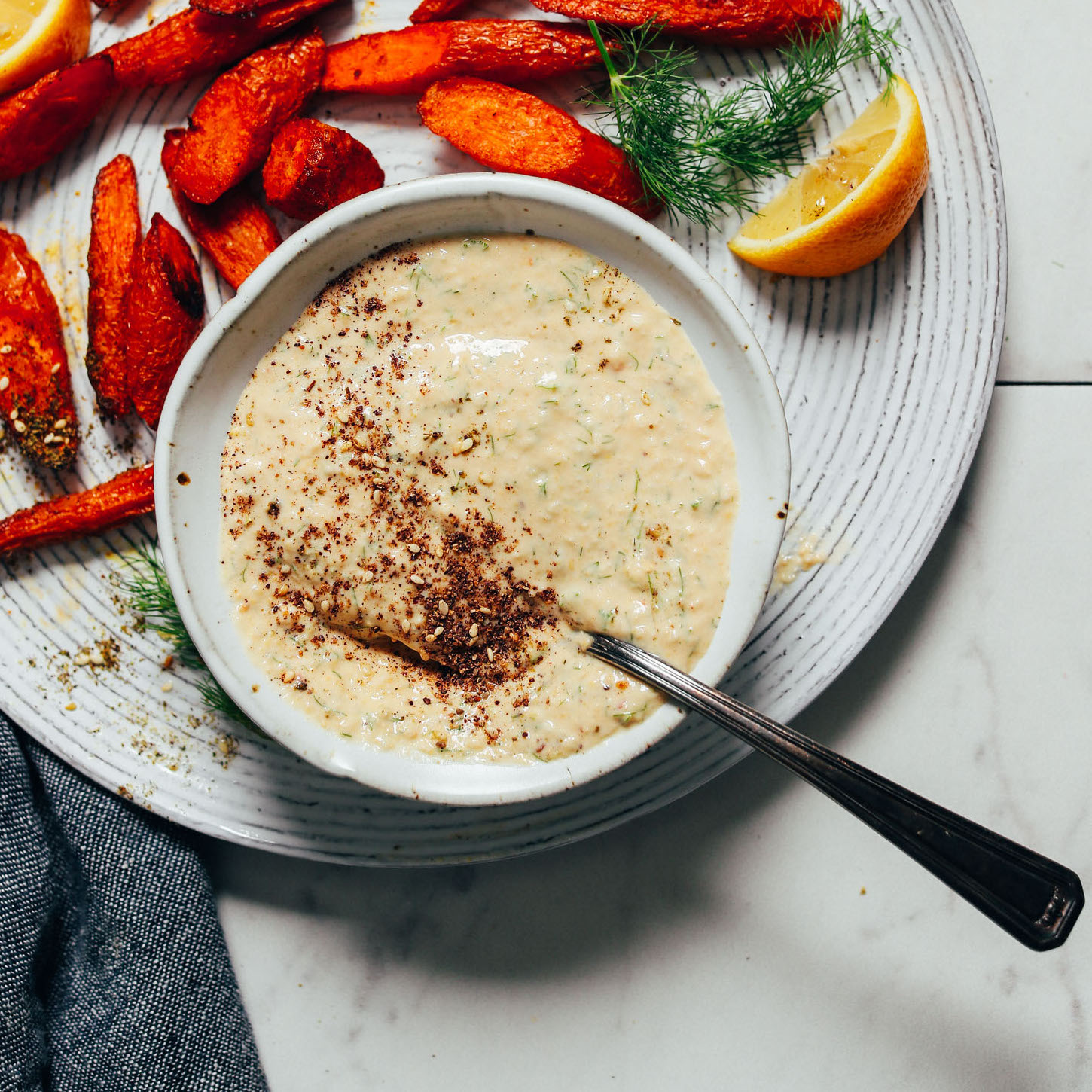 roasted carrots plated with a bowl of creamy garlic dill sauce and a fresh dill and lemon garnish