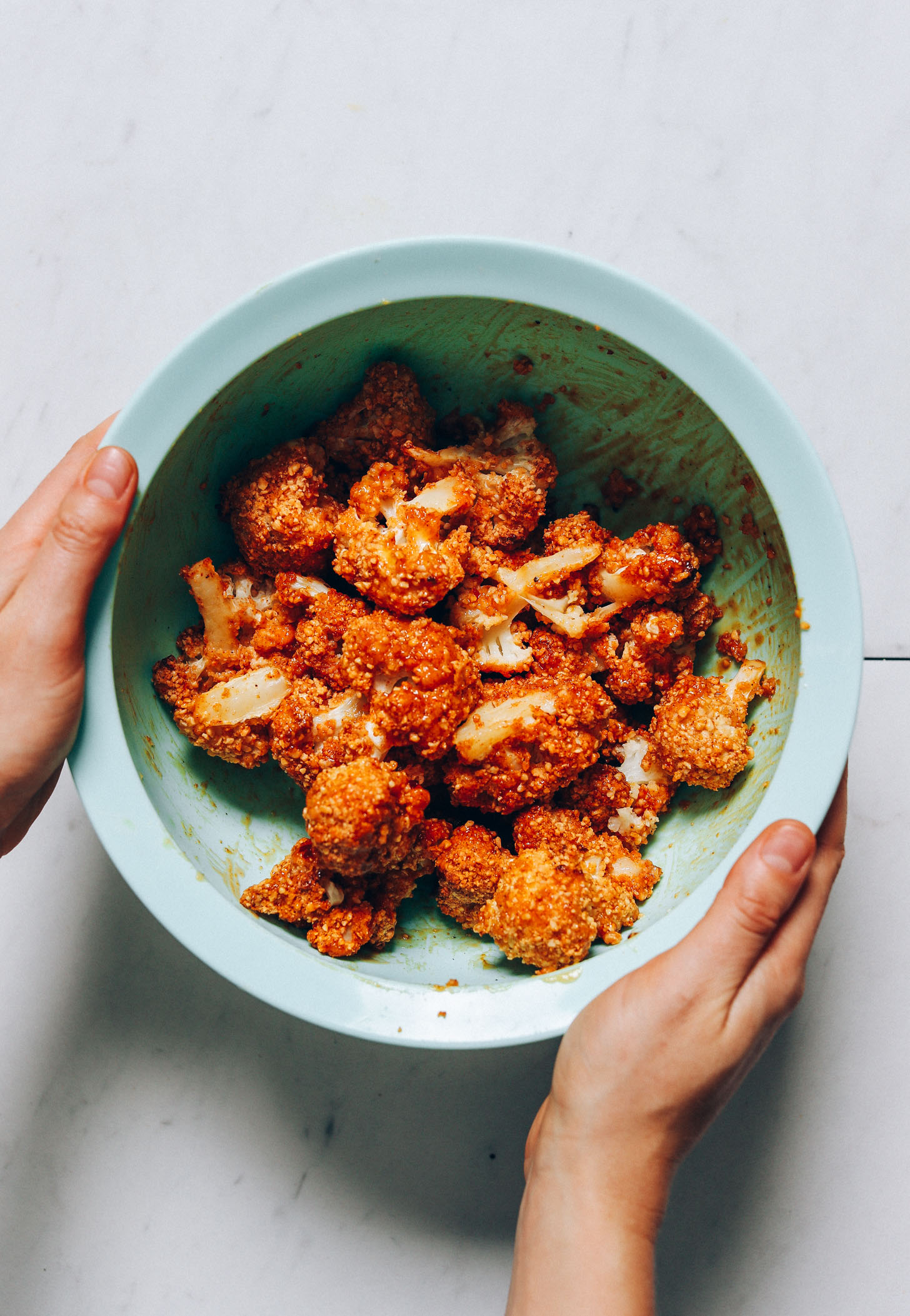Holding the sides of a bowl of Crispy Breaded Cauliflower Wings topped with a sweet and spicy glaze