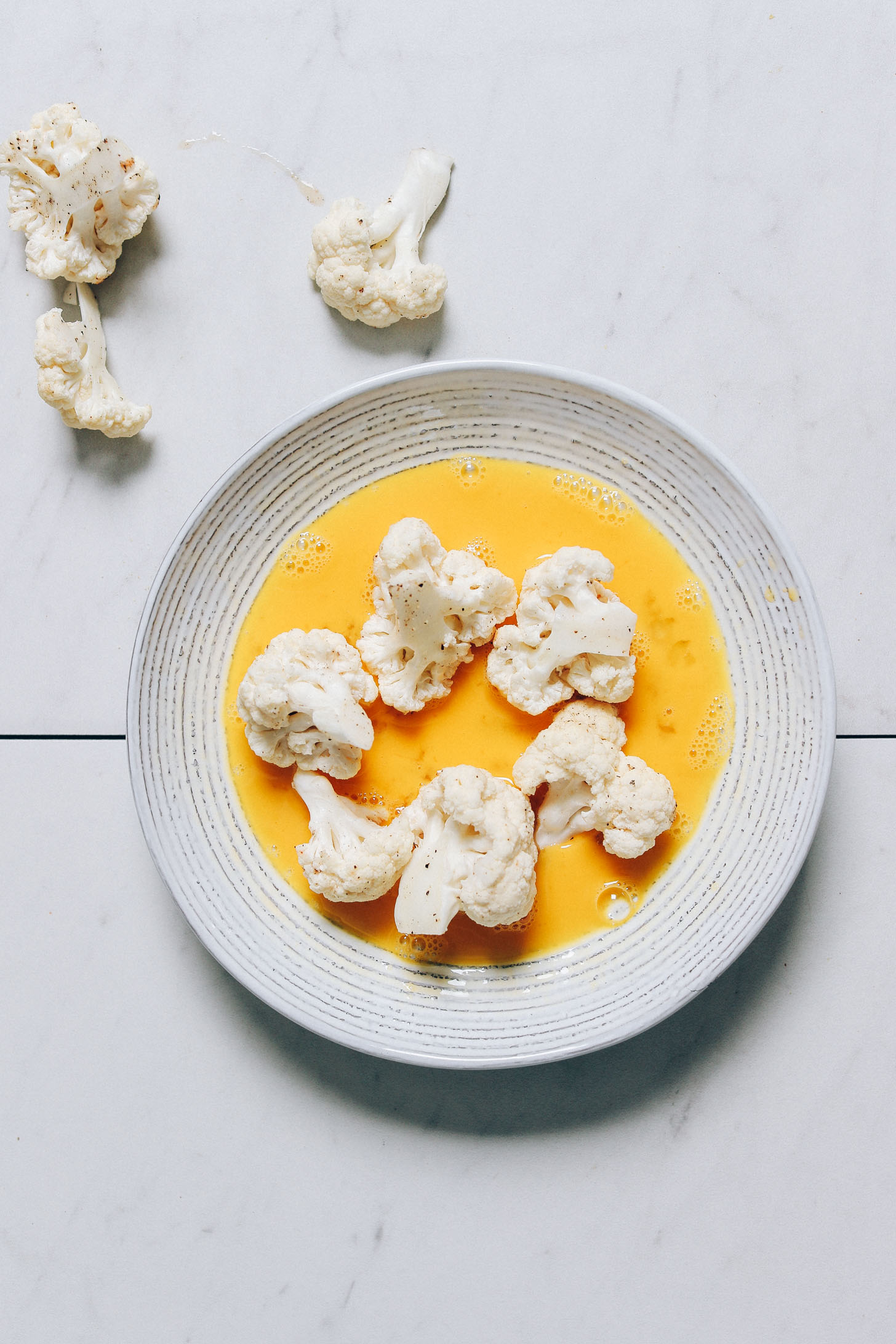 Cauliflower florets in a bowl of raw egg to help the cashew batter stick