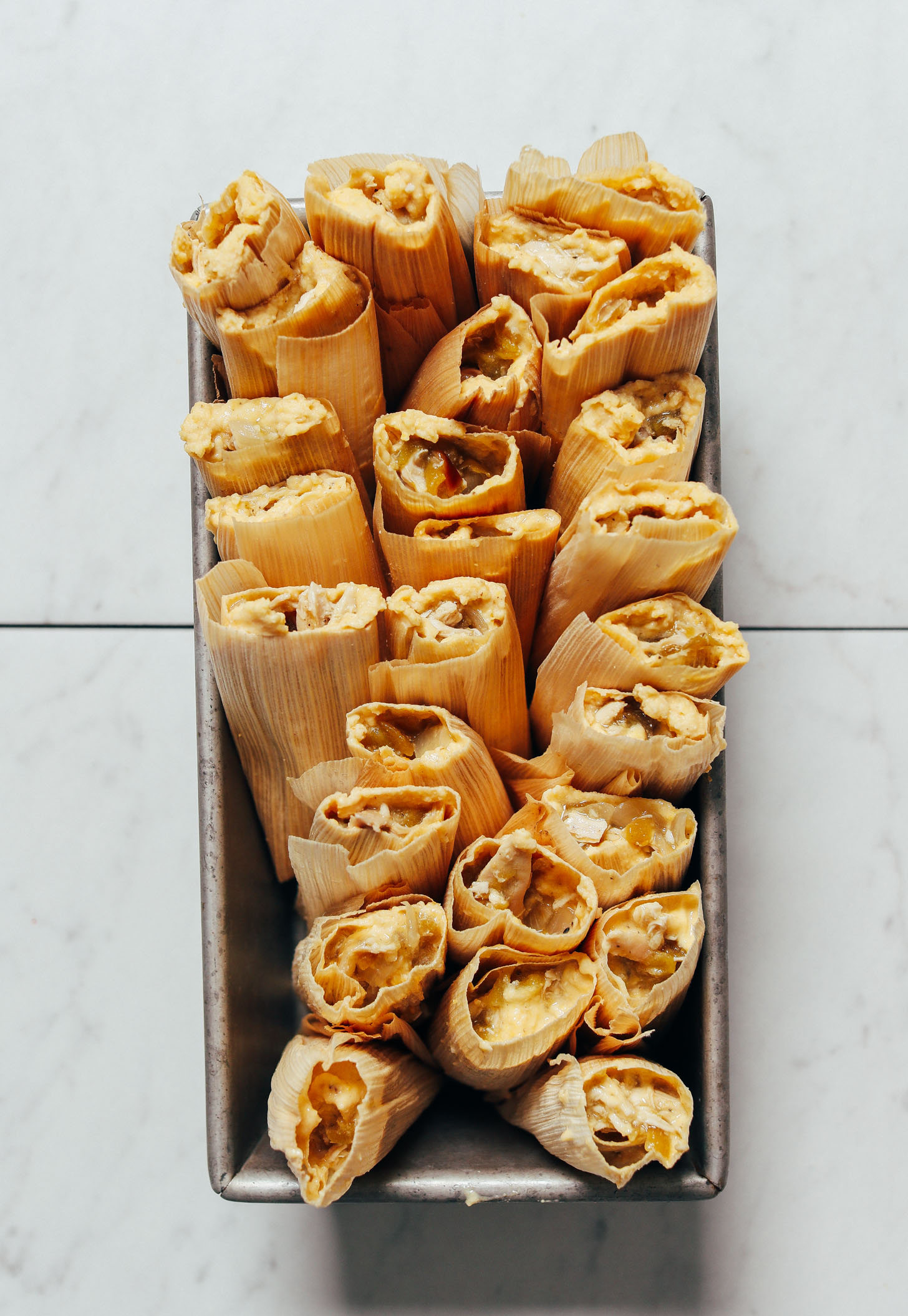 Overhead image of 26 green chile chicken tamales sitting upright in a loaf pan, uncooked