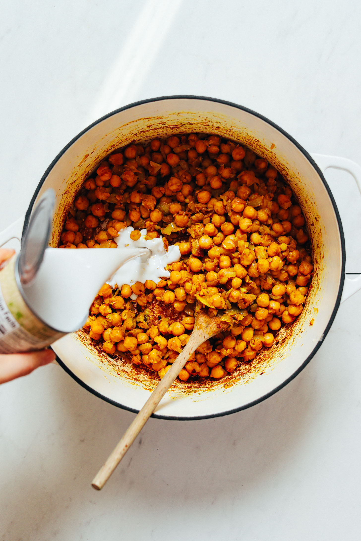 Pouring a can of coconut milk into a pot of Curried Chickpea Soup