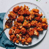 Spoon resting on a plate of Crispy Breaded Cauliflower made with a cashew-based breading