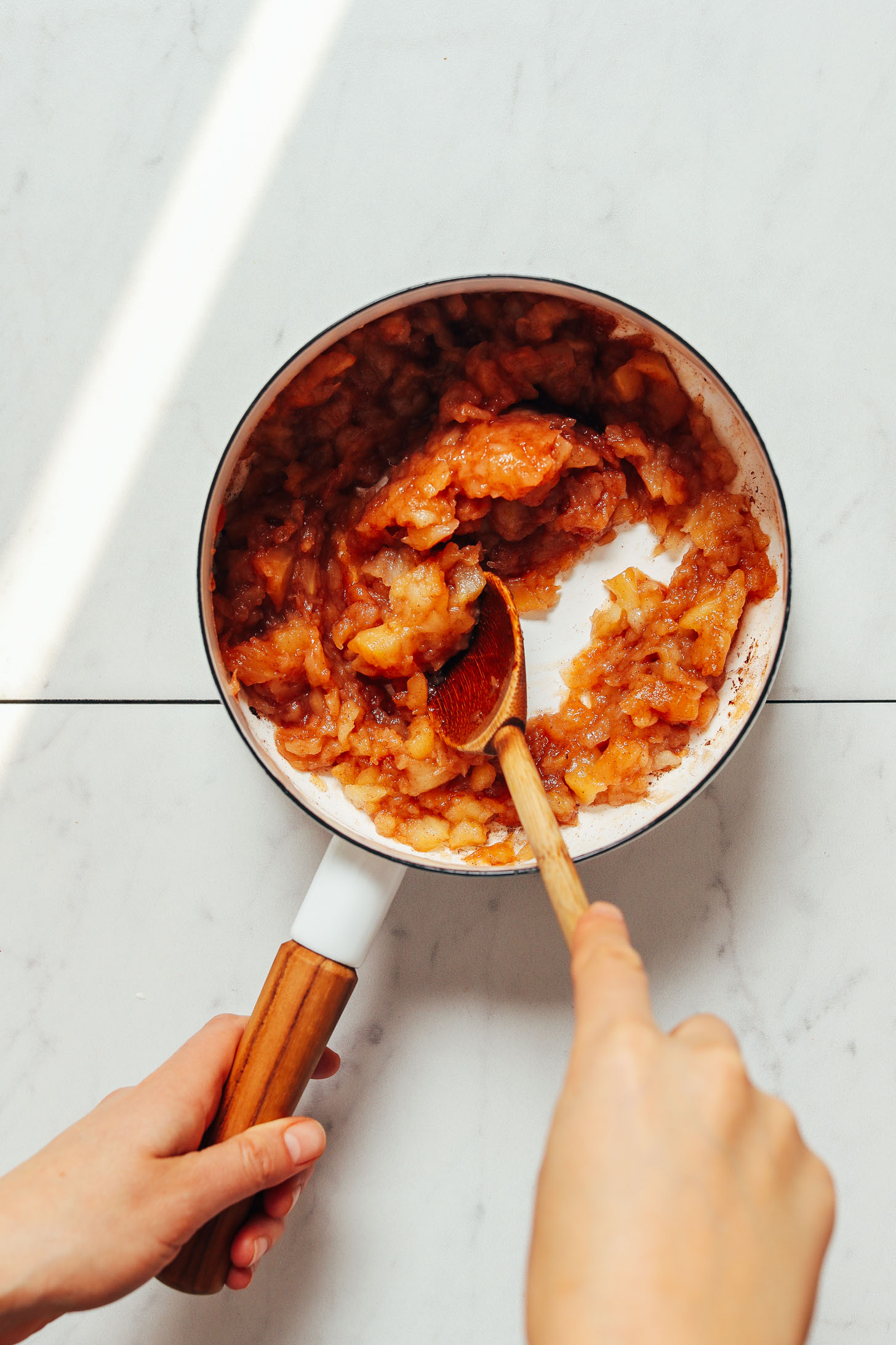 Using a wooden spoon to stir a pot of homemade unsweetened applesauce