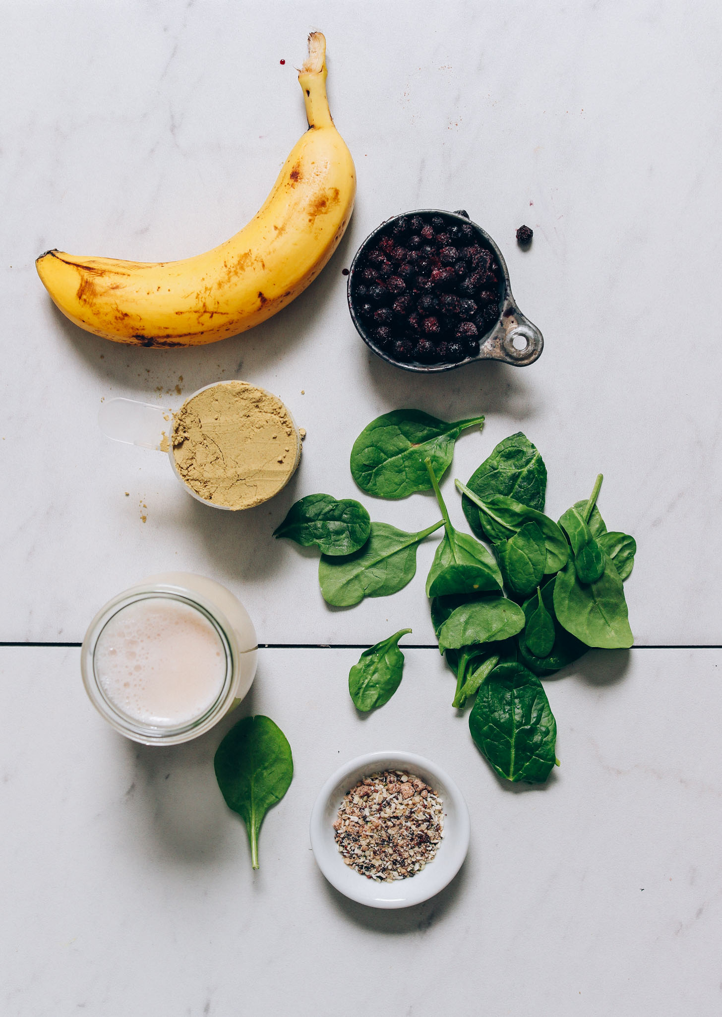 Banana, blueberries, Amazing Grass protein powder, spinach, dairy-free milk, and seeds for making a delicious smoothie