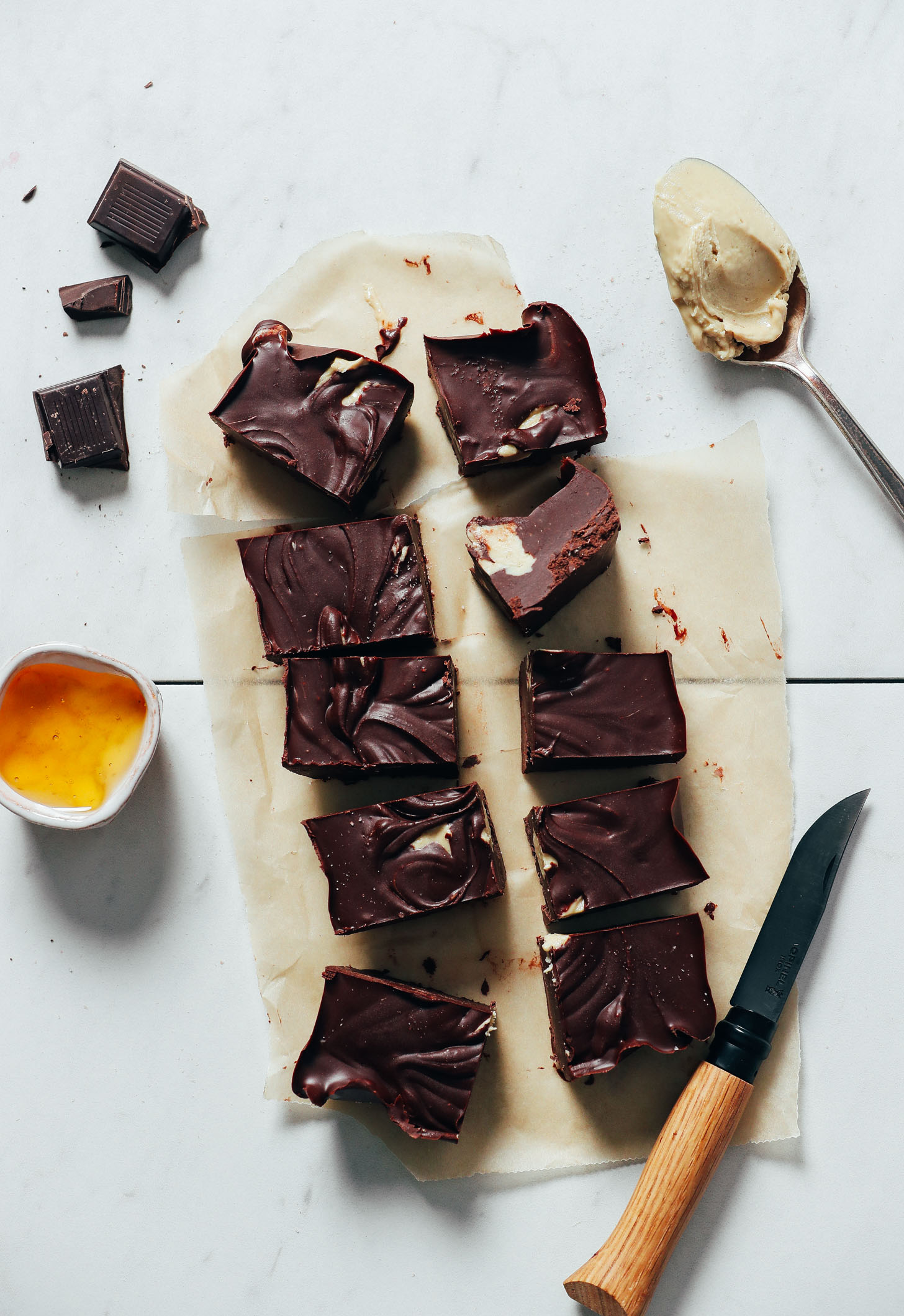 Squares of Chocolate Fudge on a piece of parchment paper next to honey, cashew butter, and dark chocolate