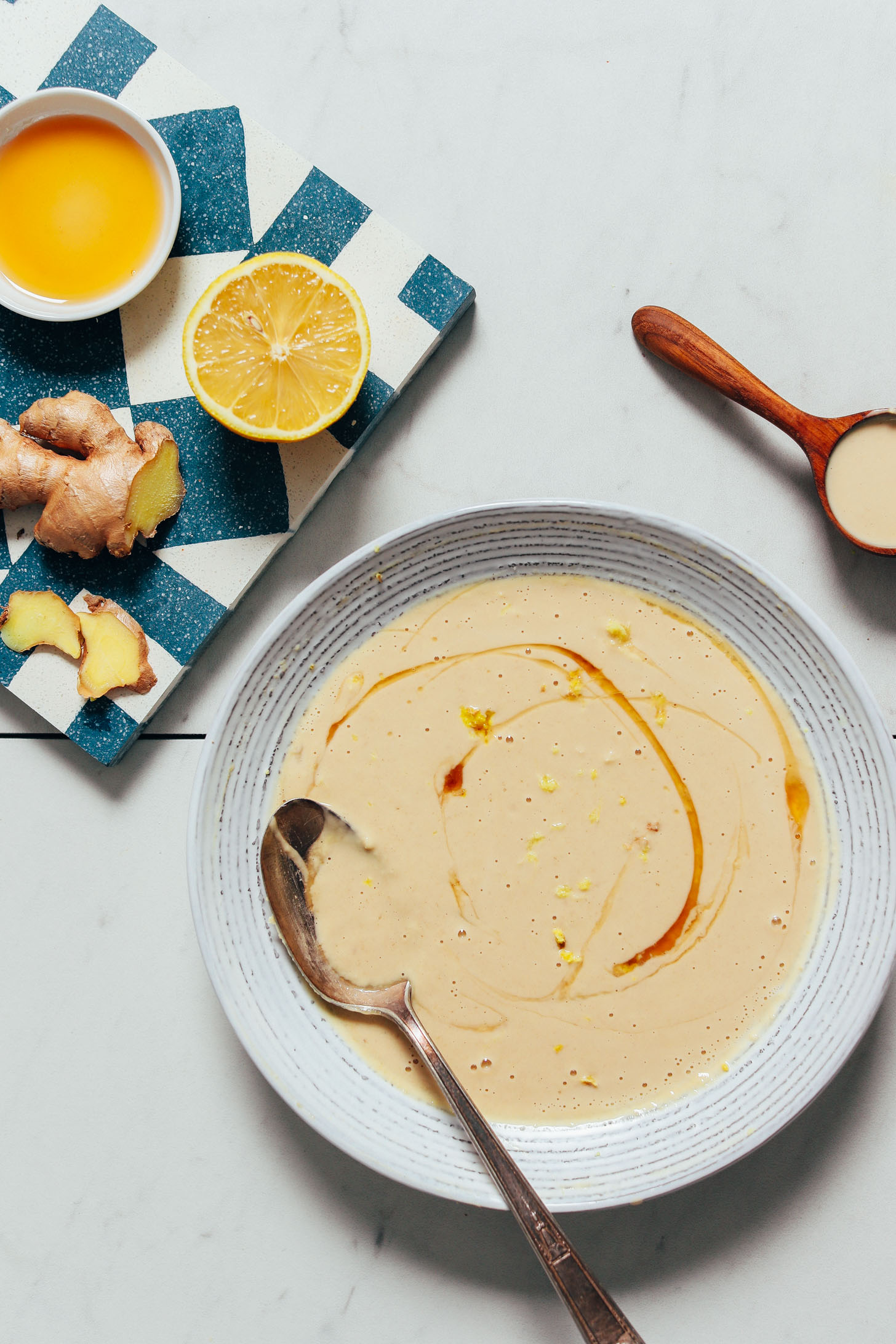 Lemon half, sliced ginger, maple syrup, and tahini beside a bowl of our Gingery Lemon Tahini Sauce recipe