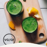 Two glasses of our Easy Green Juice recipe on a cutting board beside ingredients used to make it