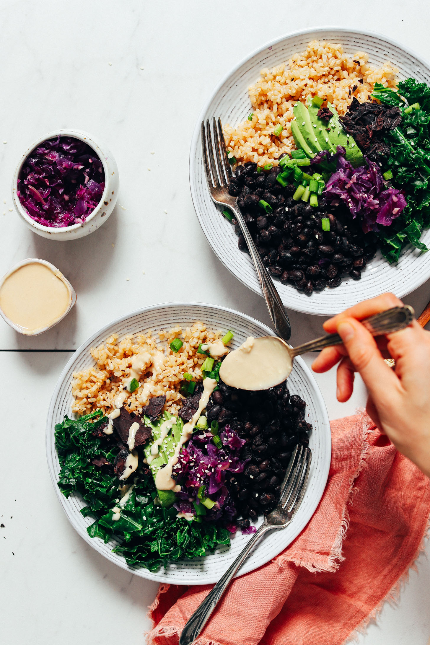 Using a spoon to top Black Bean Buddha Bowls with Lemon Ginger Tahini Sauce