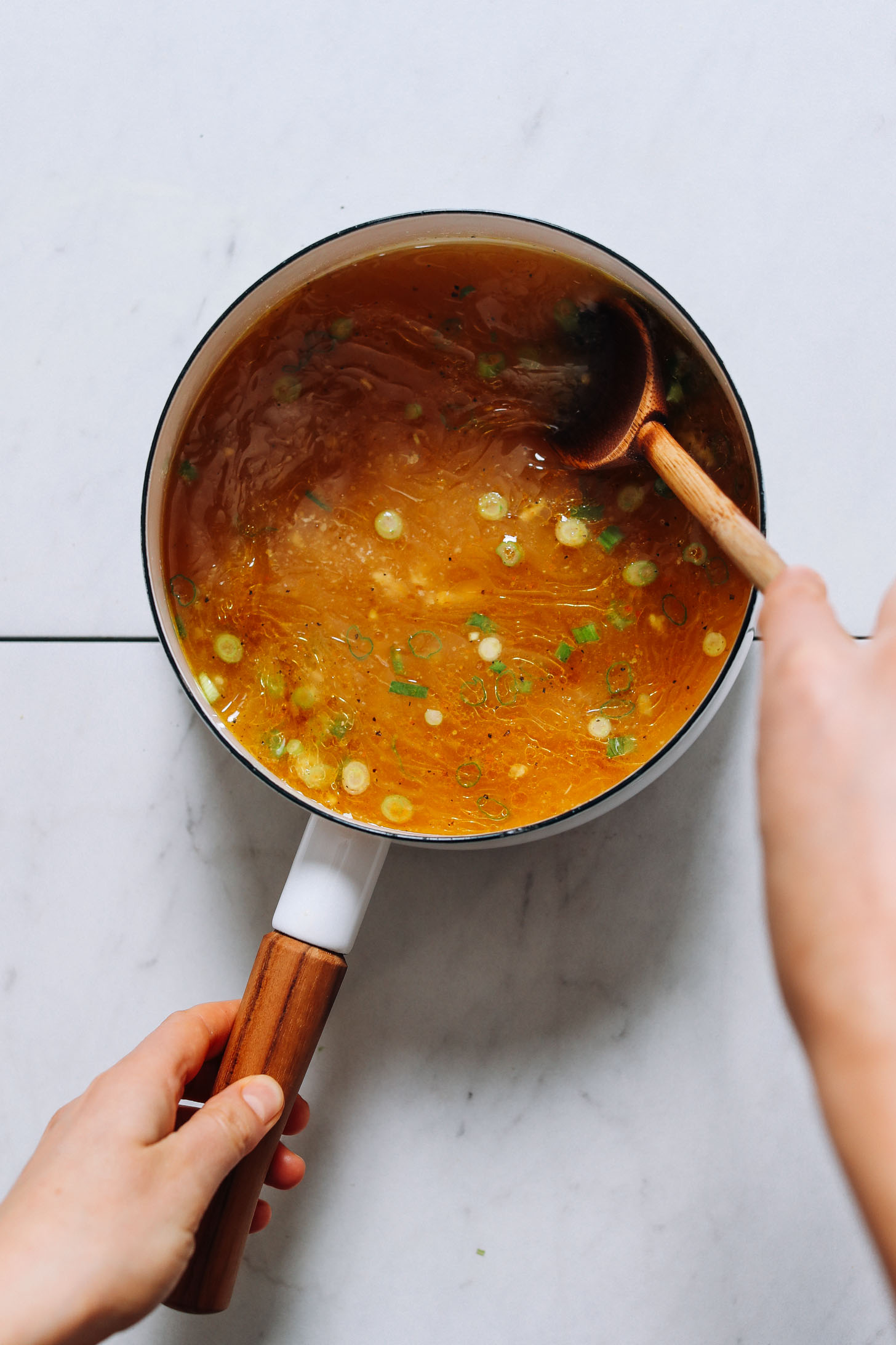Stirring green onions into a bone broth tonic