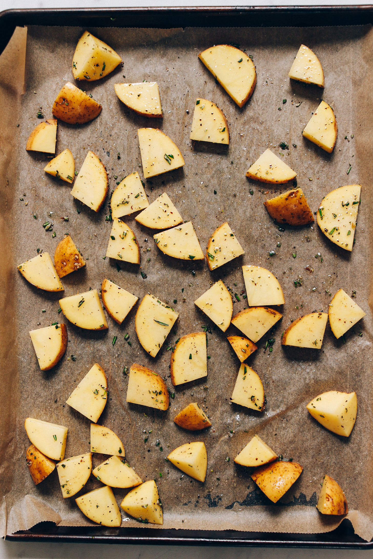 Parchment-lined baking sheet with chopped potatoes for making Crispy Roasted Potatoes