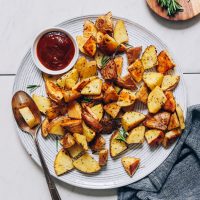 Spoon resting on a plate of Roasted Potatoes with a bowl of ketchup
