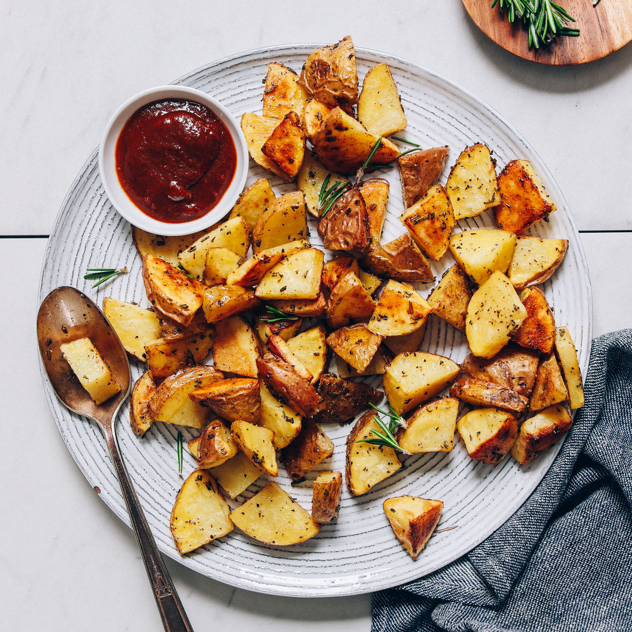Spoon resting on a plate of Roasted Potatoes with a bowl of ketchup