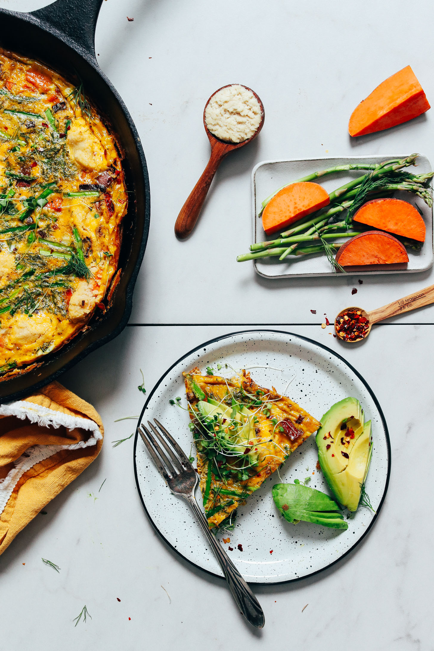 Skillet and slice of our Spring Vegetable Frittata with the slice topped with avocado, red pepper flake, and microgreens