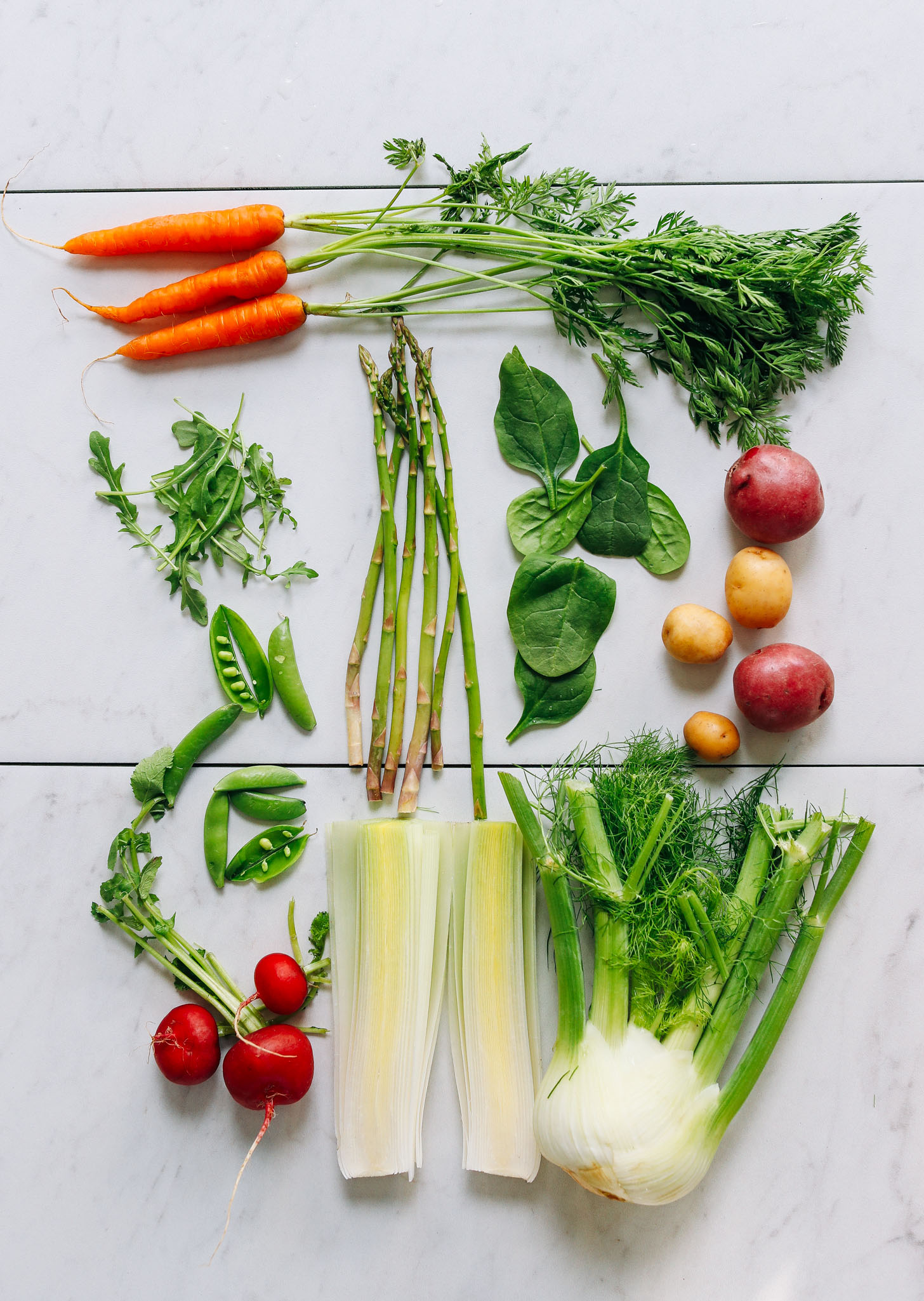 Assortment of spring vegetables including carrots, asparagus, spinach, potatoes, and more