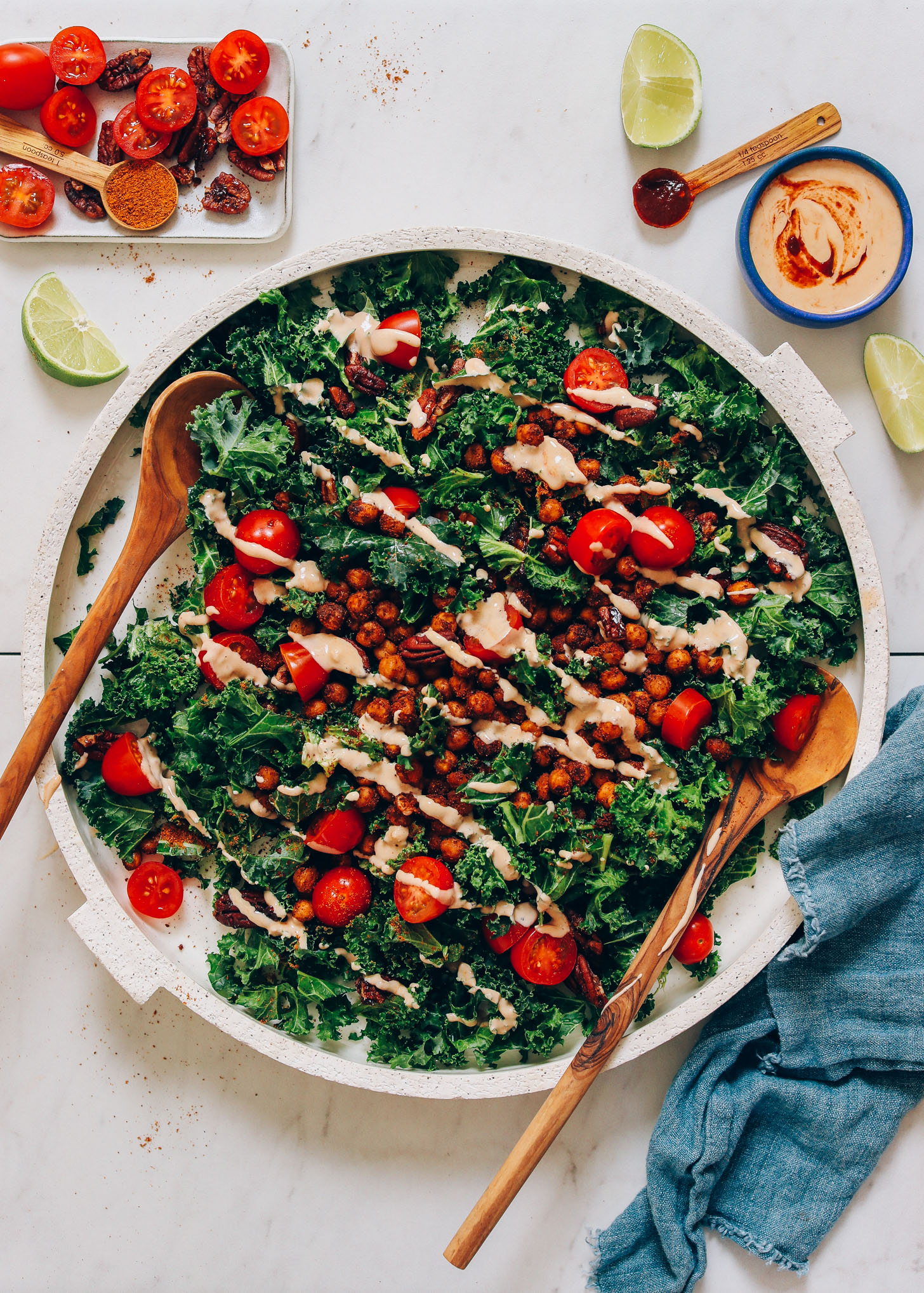 Wooden salad spoons resting on a platter of our Chickpea Chopped Kale Salad with Adobo Dressing