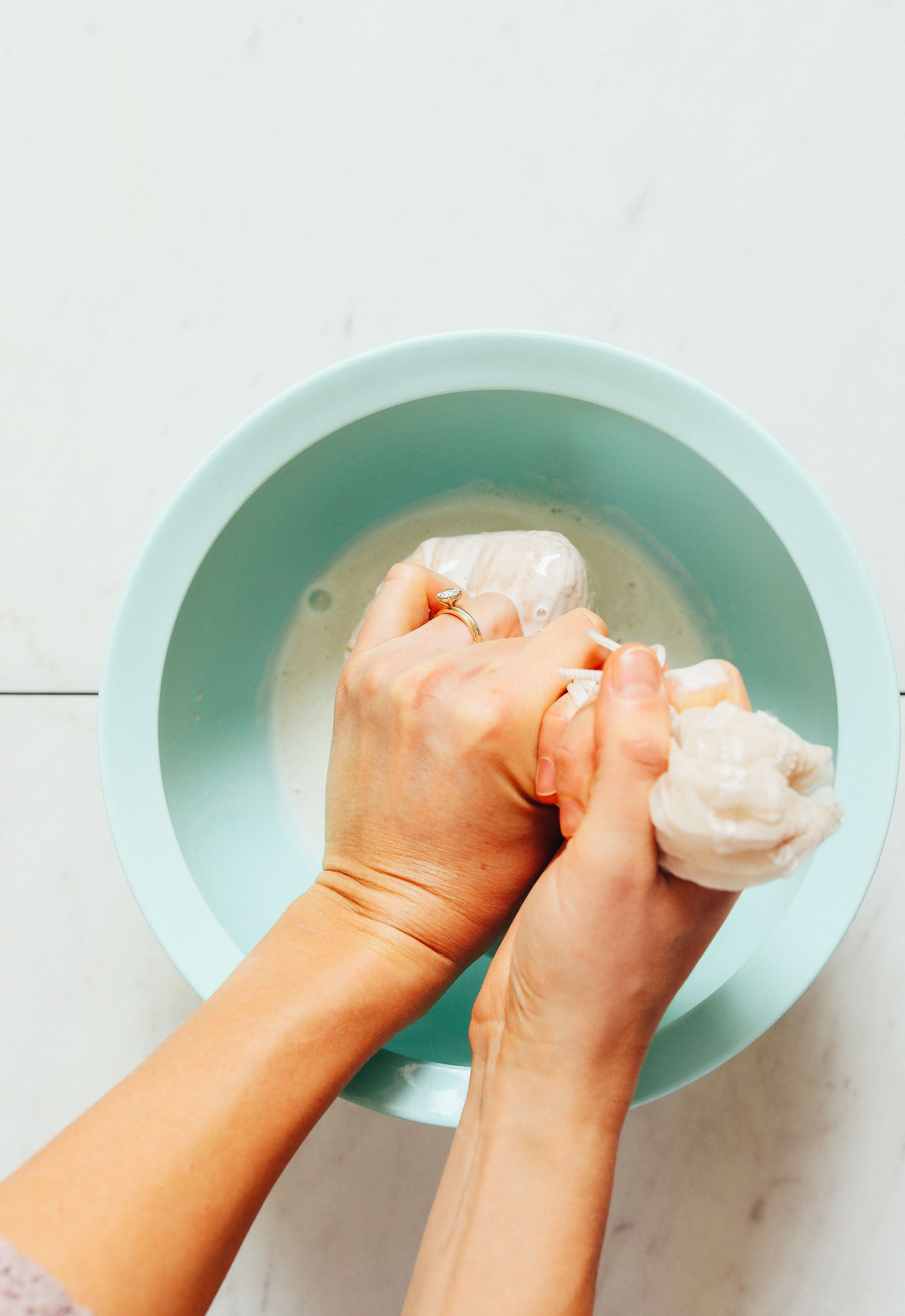 Squeezing almond milk through a nut milk bag into a bowl