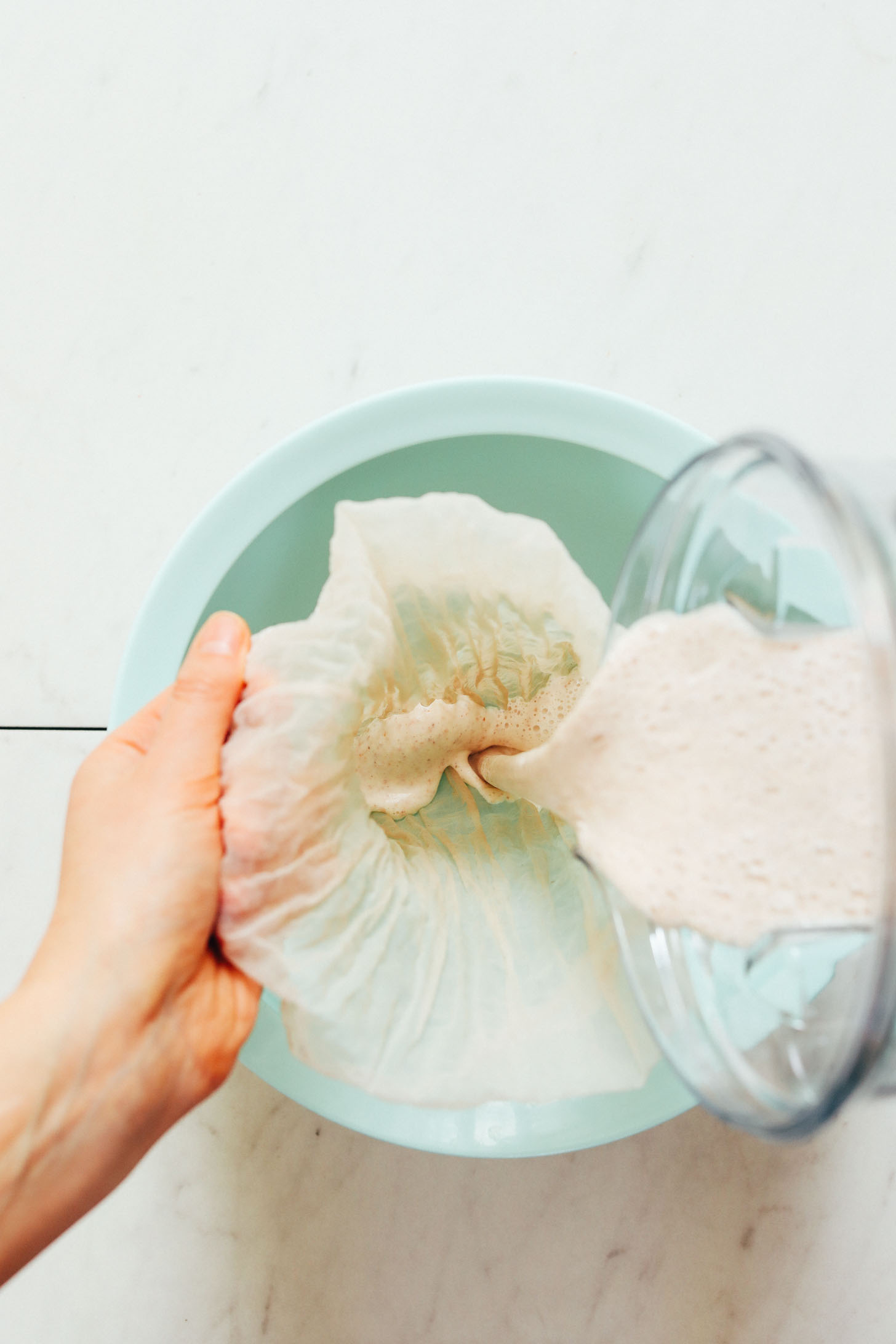 Pouring almond, water, and date mixture through a nut milk bag to make Homemade Coffee Creamer
